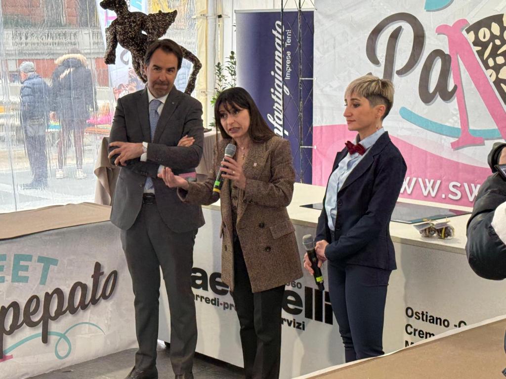 Three speakers at an event, one holding a microphone and speaking, while the others listen attentively. A decorative leopard figure is placed on the speaker's head in the background.