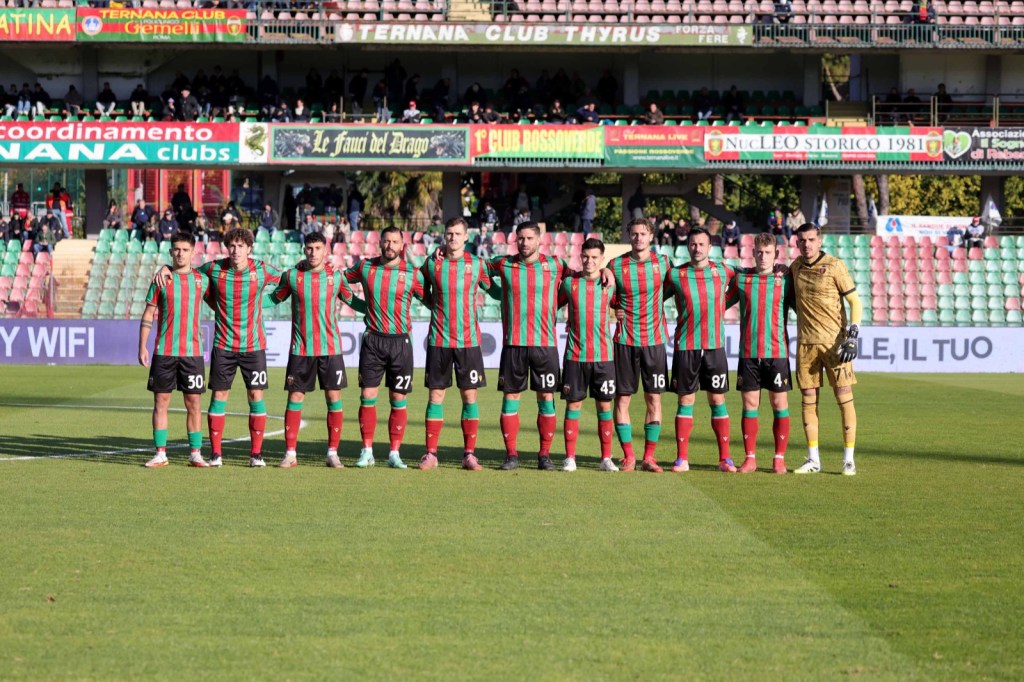 Una squadra di calcio in posa, indossando maglie a strisce rosse e verdi, con il portiere a destra in uniforme dorata, sul campo da gioco.