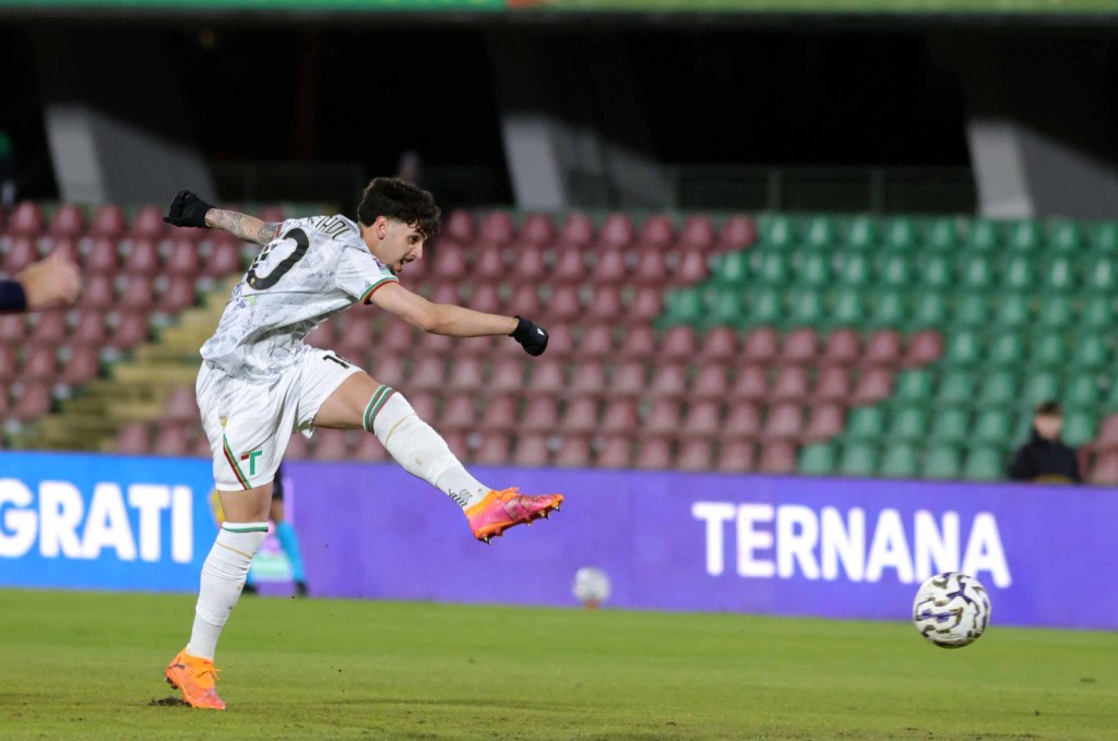 A soccer player in white and green uniform kicking a ball during a match.