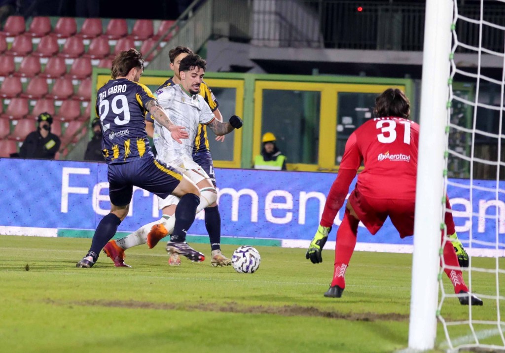 A soccer match scene showing a goalkeeper in red, players in blue and yellow jerseys, and an oncoming attack on the goal.