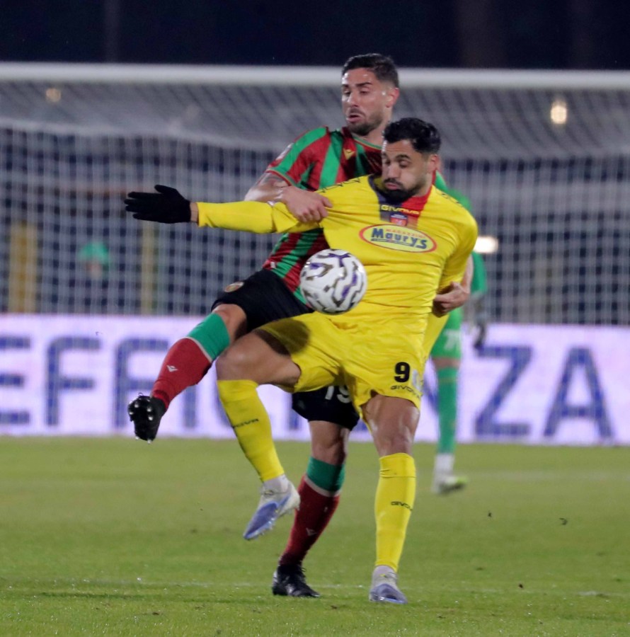 Two soccer players contesting for the ball, one in a yellow jersey and the other in a green and red striped jersey, during a match.