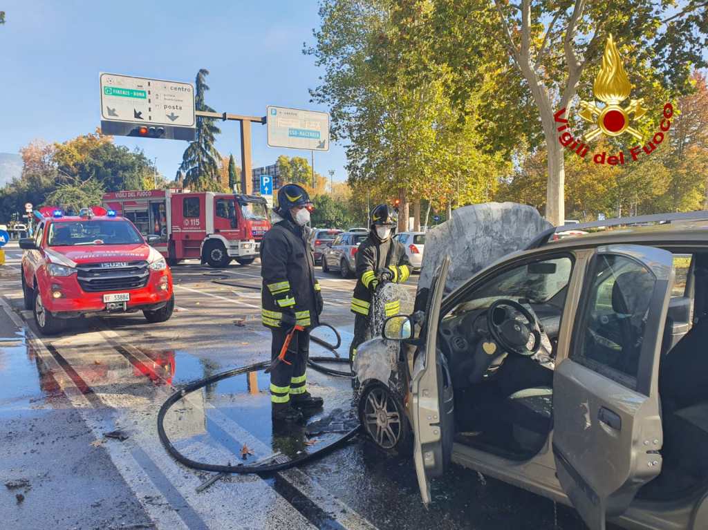 Firefighters responding to a car fire on a busy street, with emergency vehicles and traffic signs in the background.