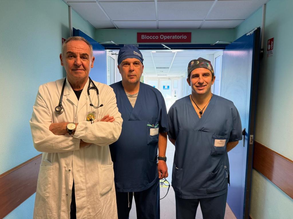 Tre medici nel blocco operatorio dell'ospedale di Perugia, indossando camici e abbigliamento da sala operatoria.