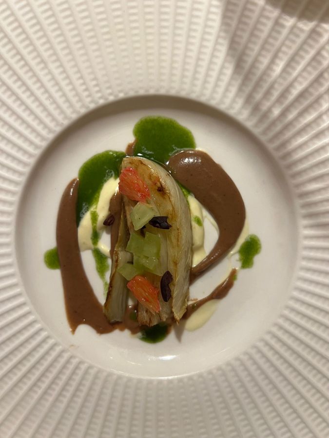 Un piatto gourmet con verdure e salse, presentato su un piatto bianco decorato con motivi concentrici.