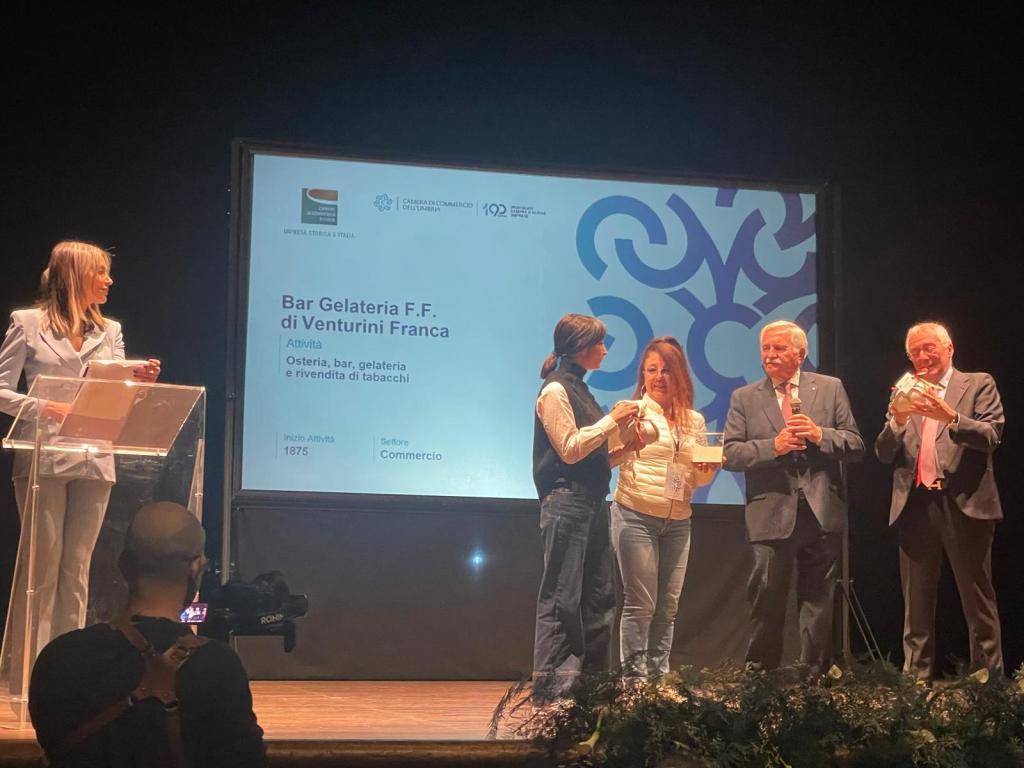 Cerimonia di premiazione per Bar Gelateria F.F. di Venturini Franca, con relatori e rappresentanti sul palco, in un teatro.