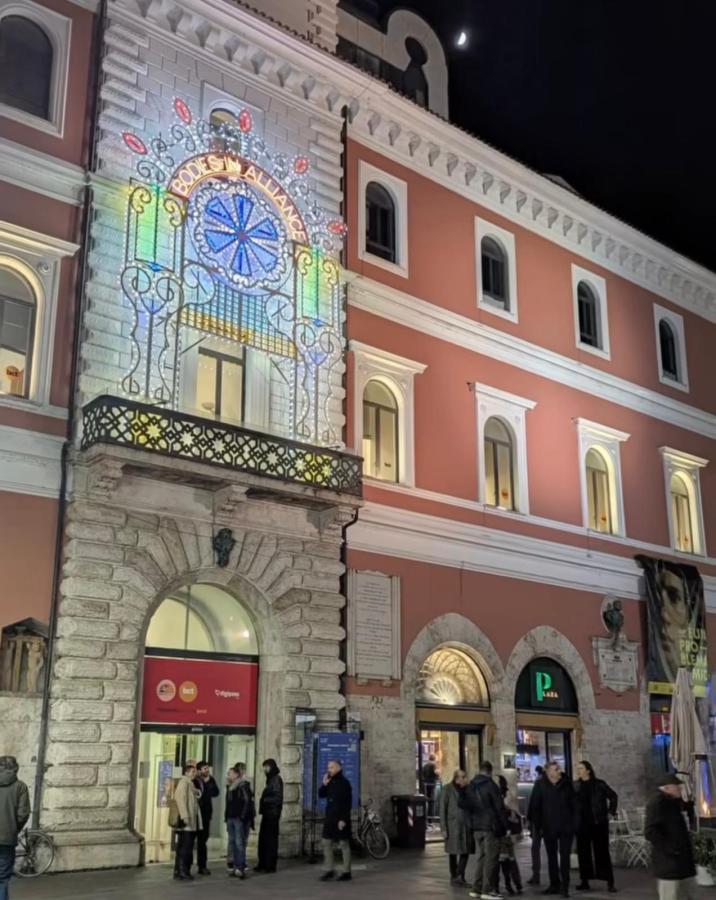 View of a historic building at night, adorned with colorful light projections reading 'BODE'S ALLIANCE'. Several people are gathered in front of the entrance.