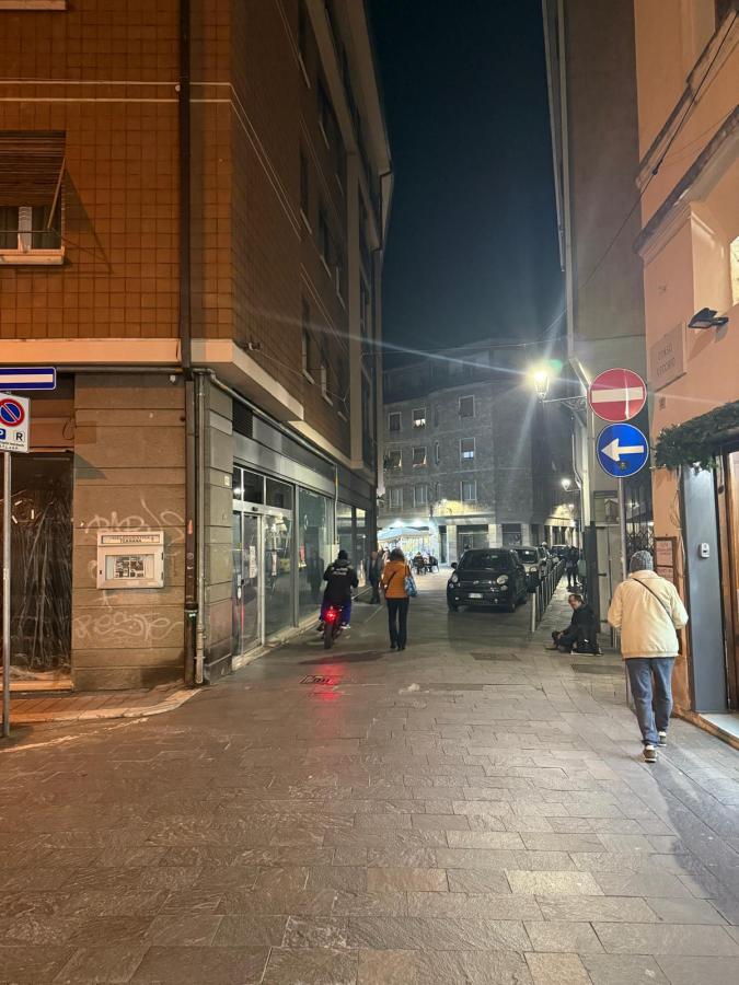 A narrow street at night with a pedestrian and a cyclist, surrounded by buildings and illuminated by streetlights.