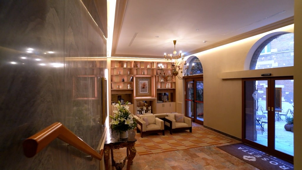 Interno di un hotel a Perugia con un'accogliente area salotto, pareti in marmo e scaffali ben curati, illuminato da luci soffuse e decorato con fiori freschi.