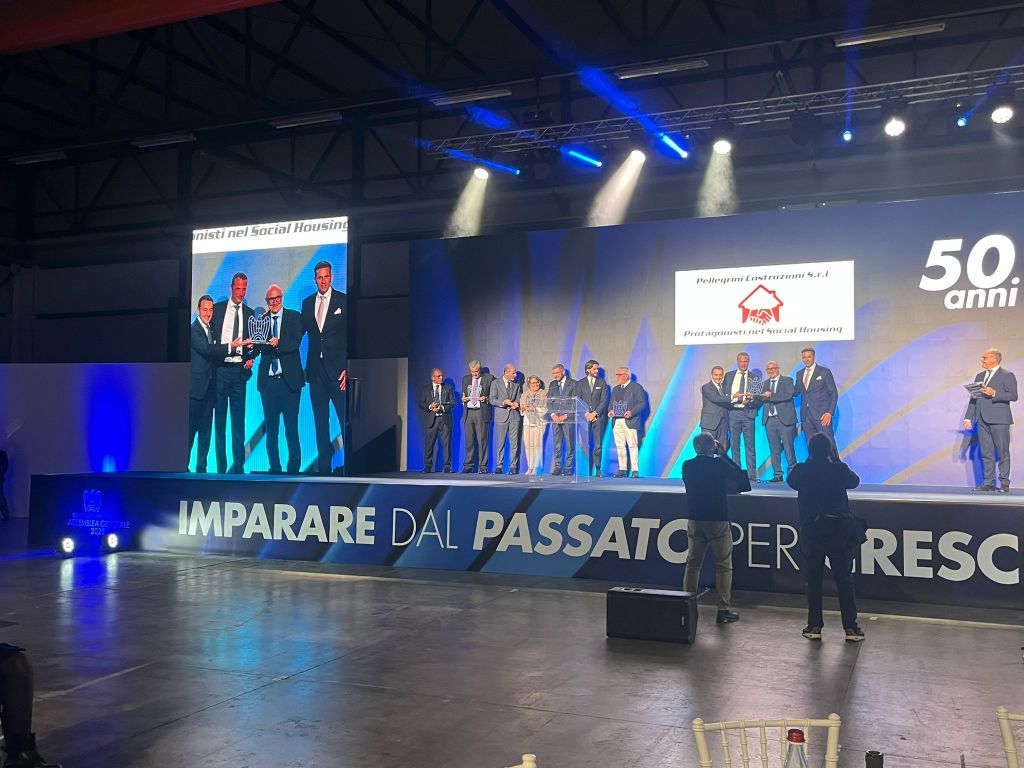 Cerimonia di premiazione con un gruppo di persone sul palco che ricevono riconoscimenti per la loro lunga appartenenza a Confindustria, con sfondo di luci blu e scritte commemorative.