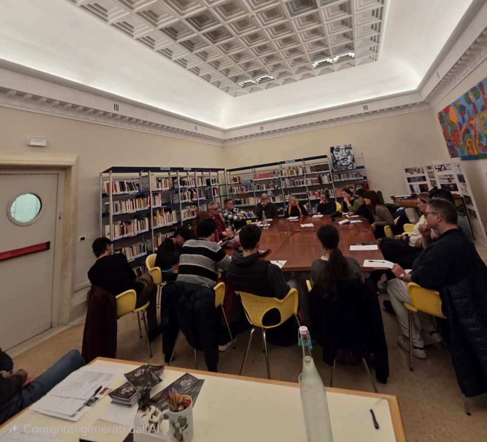 Gruppo di partecipanti a un workshop di scrittura creativa in una sala della biblioteca, con tavolo centrale e scaffali di libri sullo sfondo.