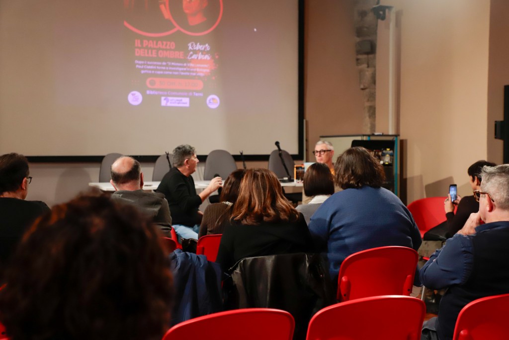 Un evento al Terni e Narni Horror Fest con un autore in discussione su un palco, mentre il pubblico ascolta attentamente seduto in poltrone rosse.
