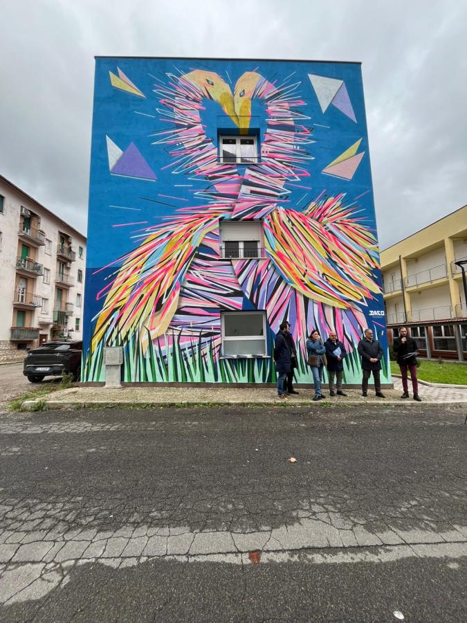 Murales intitolato 'GRAFFAUNE AMOUR' realizzato dall'artista DACO, raffigurante una coppia di cigni con i colli intrecciati a formare un cuore. L'opera si trova su un edificio a Terni, caratterizzata da colori vivaci e forme geometriche che richiamano l'architettura urbana.