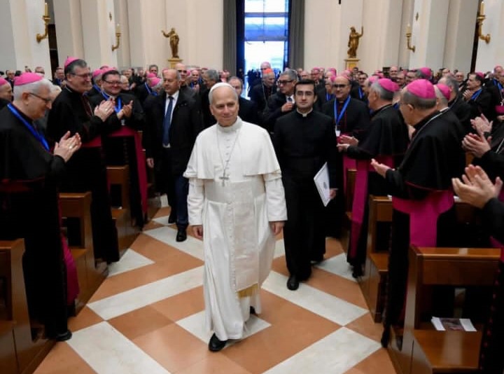Papa Leone XIV cammina tra i partecipanti dell'assemblea generale, accolto da applausi in una sala affollata di vescovi e sacerdote.