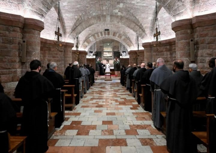 Vista interna di un luogo di culto con numerosi frati riuniti in preghiera, in un'atmosfera solenne e raccolta.