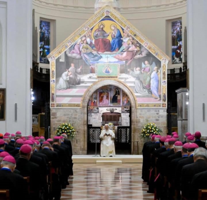Il Papa Leone XIV parla in una chiesa, con un gruppo di vescovi in abiti formali che ascoltano. Sullo sfondo, si vede un bel affresco sopra l'altare.