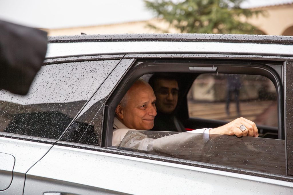 Papa Leone XIV sorride dal finestrino di un'automobile mentre piove, accogliendo i fedeli all'esterno.