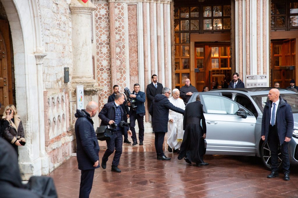 Papa Leone XIV arriva al Sacro Convento di Assisi, accolto da una folla di fedeli mentre scende da un'auto.