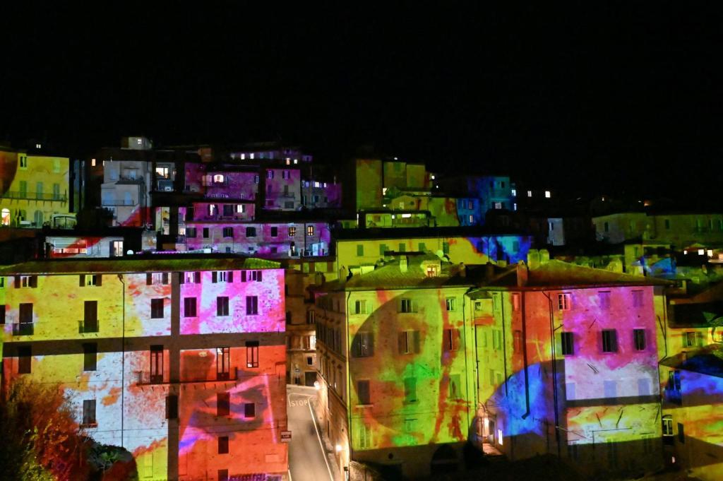 Proiezione di luci colorate su edifici storici durante l'inaugurazione delle luminarie natalizie a Perugia.