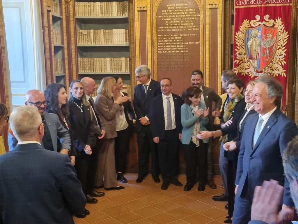 Un gruppo di persone in un ambiente accademico festeggia le nuove nomine nella governance dell'Università di Perugia, con alcuni membri che sorridono e applaudono.