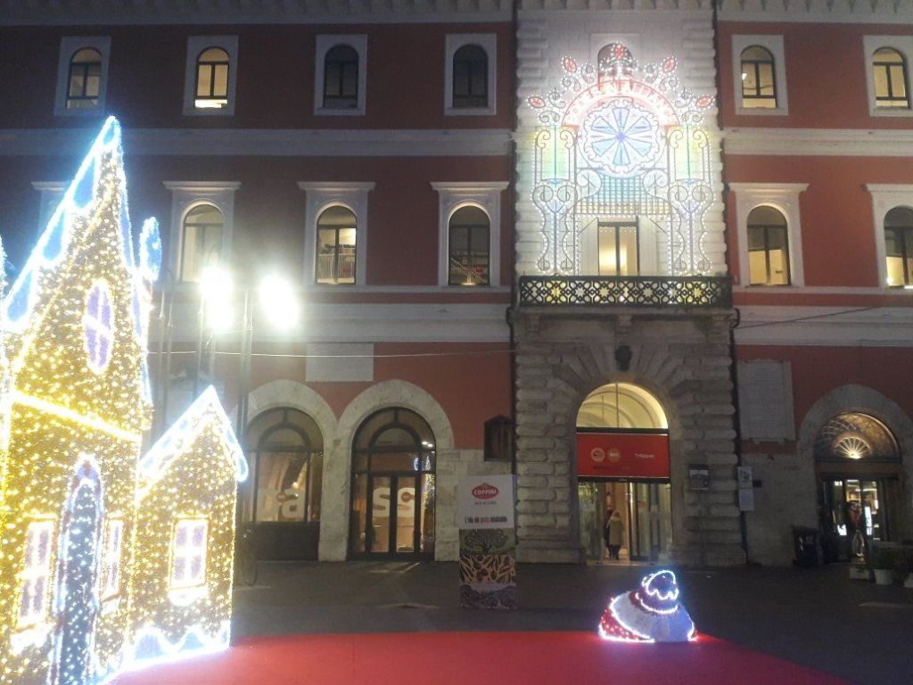 Illuminated festive decorations outside a building, featuring a stylized gingerbread house and a snowman figure, with colorful lights illuminating the facade.