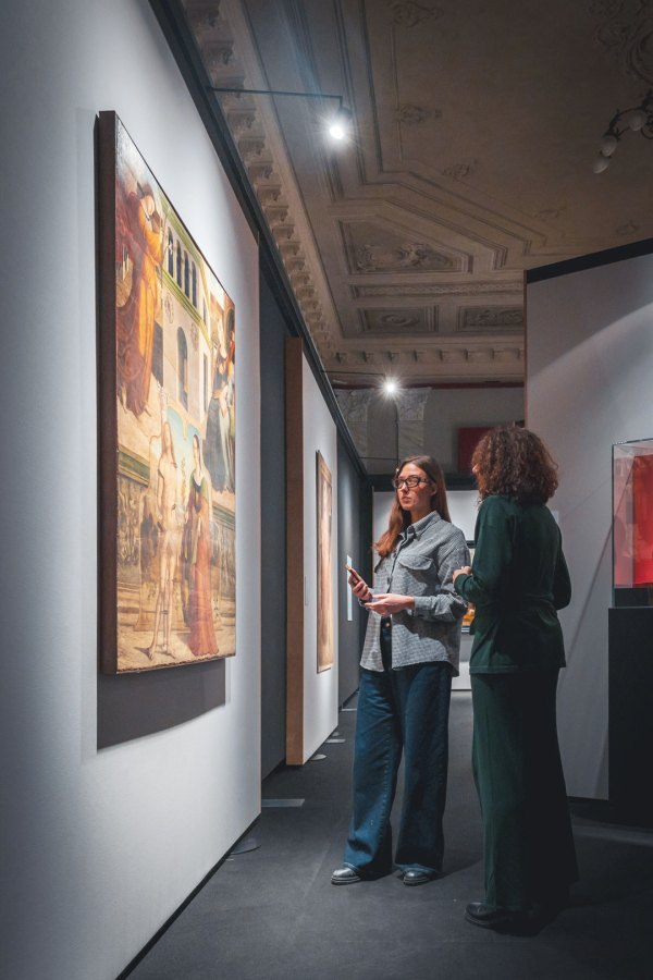 Due donne in un museo osservano un'opera d'arte mentre discutono, circondate da altre opere esposte.