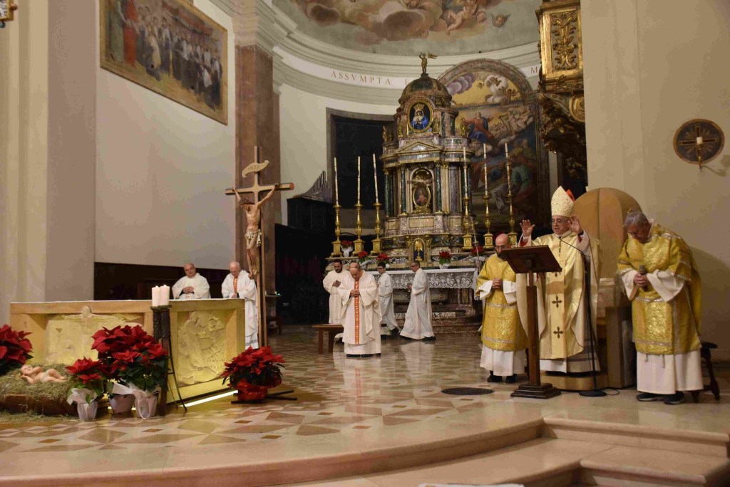 Celebrazione della Messa di Natale nella cattedrale di Terni, con il vescovo Francesco Antonio Soddu e altri sacerdoti al centro. L'altare è decorato con stelle di Natale, mentre la chiesa è adornata con elementi liturgici e dipinti sul soffitto.