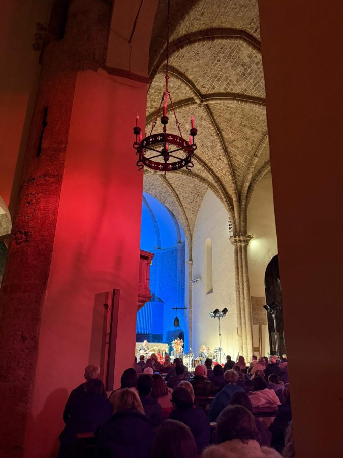 Interno della chiesa di San Francesco durante il concerto di Mario Donatone & Bluesman Latino, con il pubblico seduto e illuminazione suggestiva blu e rossa.