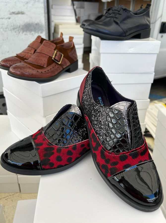 Scarpe eleganti in stile leopardato con dettagli lucidi, posizionate su una pila di scatole bianche, insieme ad altri modelli di calzature.