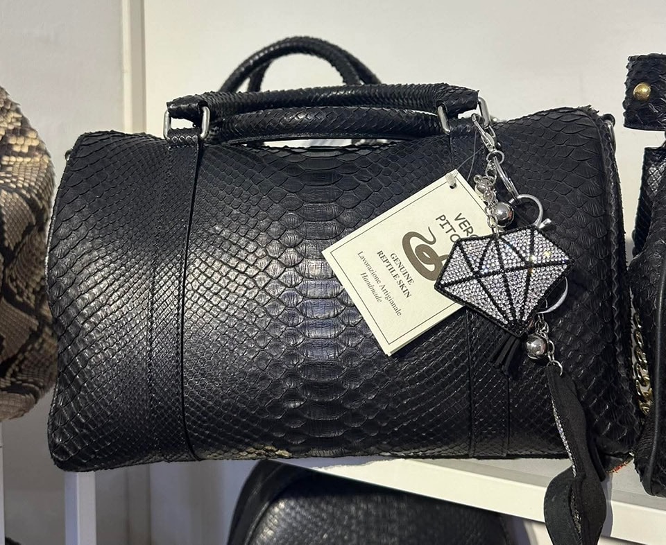 Borsa nera in pelle di serpente con etichetta che indica la provenienza e un ciondolo a forma di diamante.