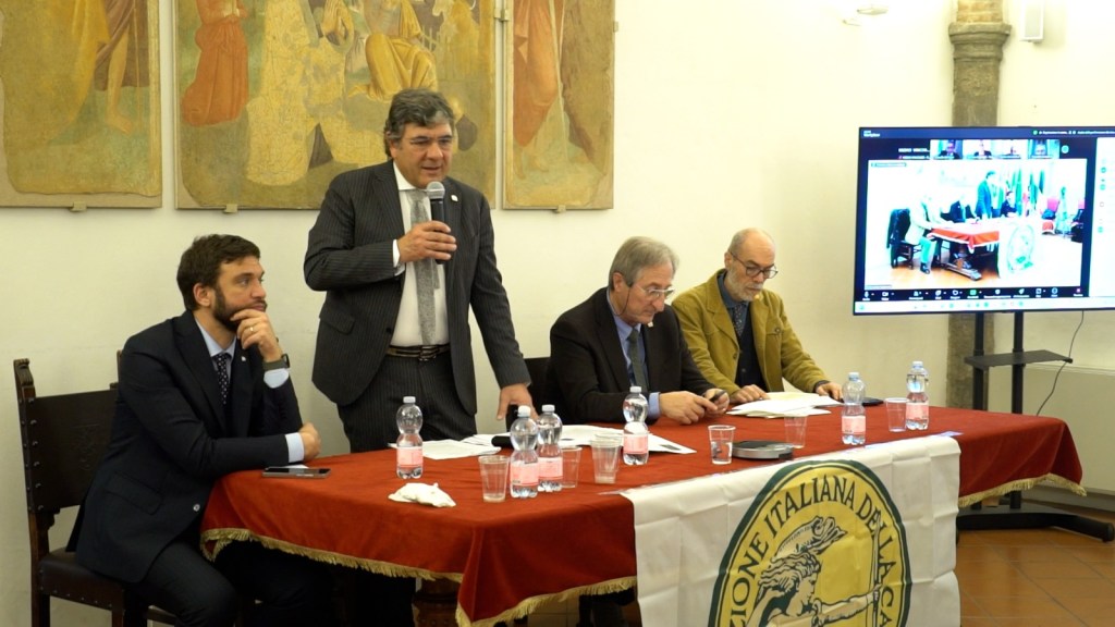Un incontro sulla Nature Restoration Law con diversi relatori, incluso un senatore, si svolge in una sala con opere d'arte alle pareti. Il tavolo è decorato con bottiglie d'acqua e una bandiera della Federazione italiana della caccia.