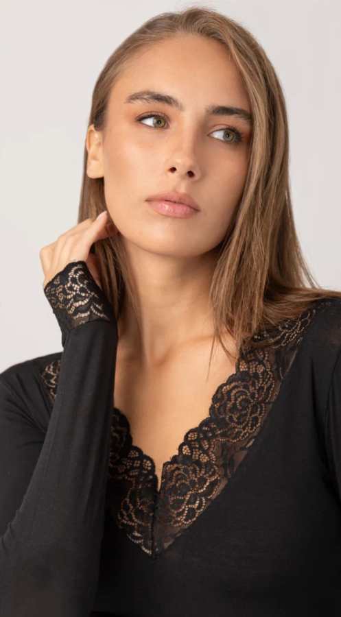 Modella con top nero con pizzo, esprimendo eleganza e stile, mentre presenta un aspetto pensieroso.