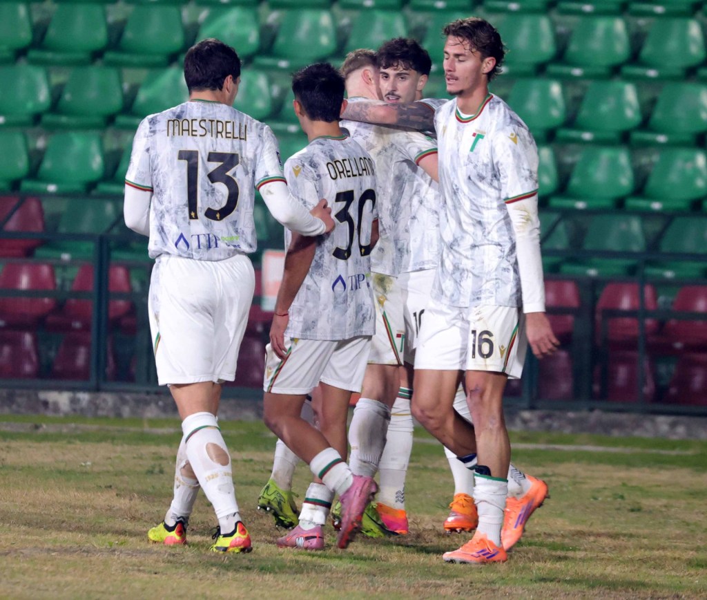 A group of football players celebrating a goal on the field, wearing white jerseys with player numbers visible.