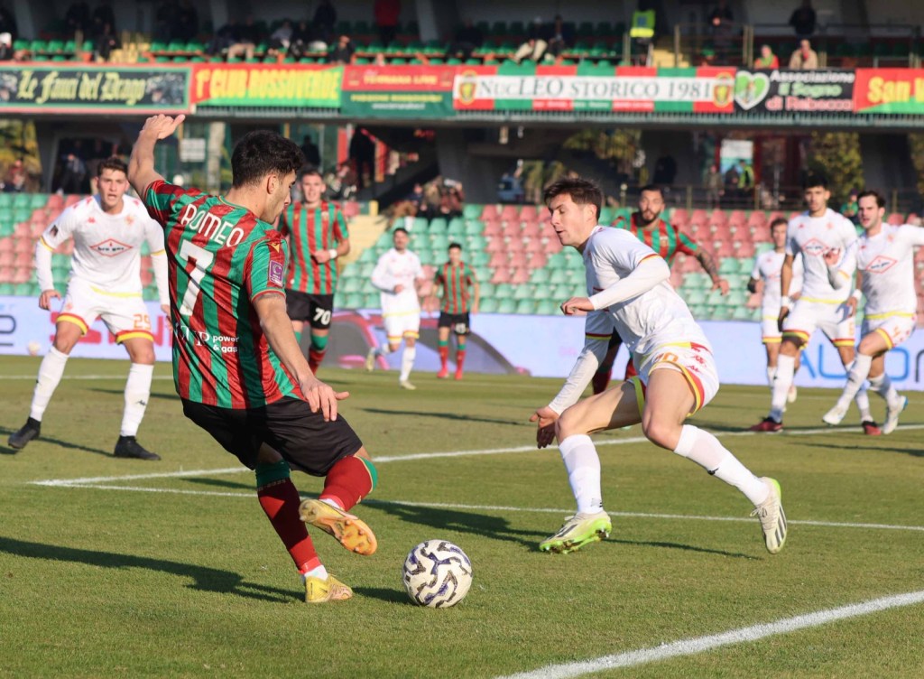 A soccer match in progress, featuring a player in a red and green striped jersey attempting to control the ball while being challenged by an opponent in a white jersey.
