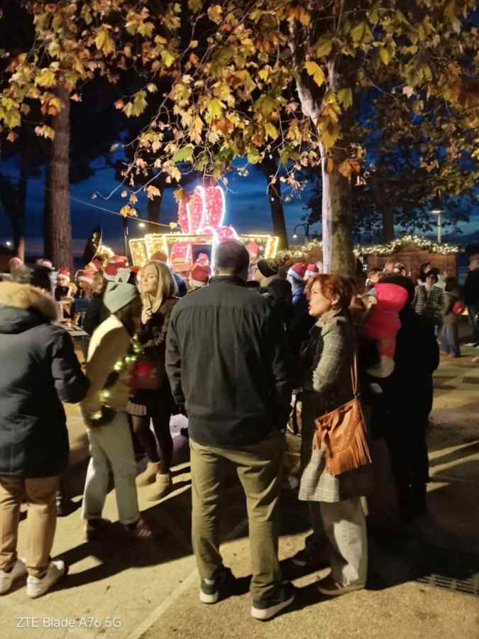 Folla entusiasta durante la parata natalizia a Passignano, con persone vestite da Babbo Natale e decorazioni luminosi sullo sfondo.