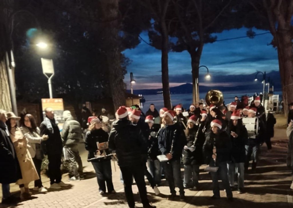 Una parata natalizia con una banda musicale e figuranti in costume, circondati da una folla entusiasta lungo il lungolago di Passignano.