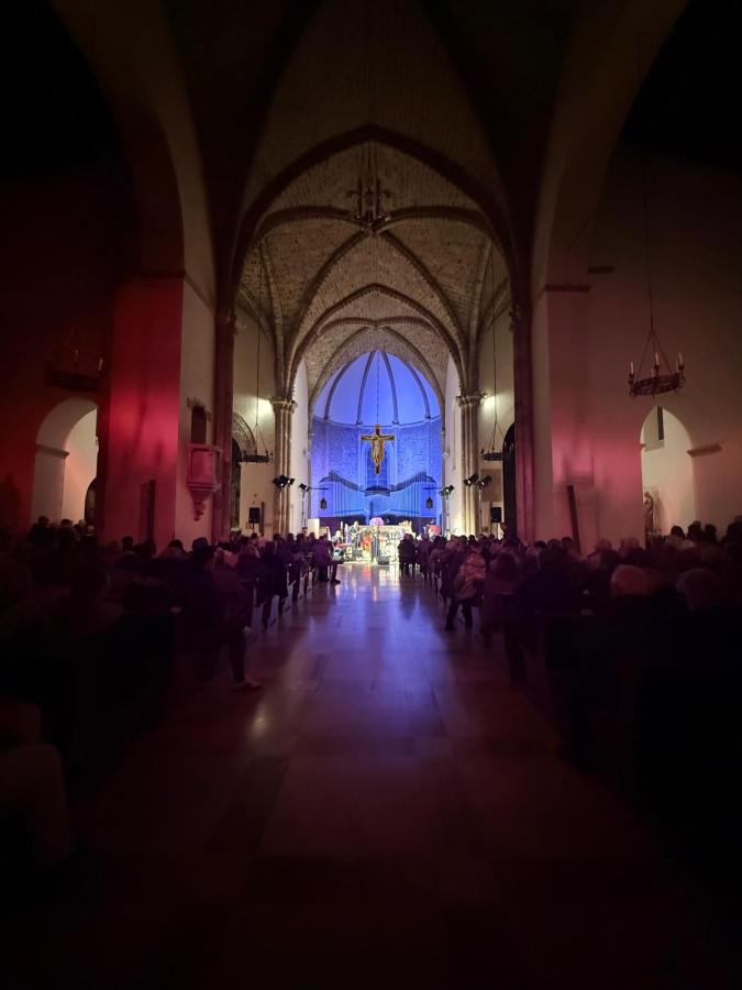 Interno della Chiesa di San Francesco durante un concerto Gospel, con una grande affluenza di pubblico e un'atmosfera suggestiva creata da luci colorate.