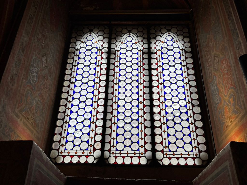 Vetrate storiche della Sala dei Notari a Perugia, con un design decorativo di vetro soffiato e piombo, caratterizzate da cerchi bianchi e blu, illuminate dalla luce naturale.