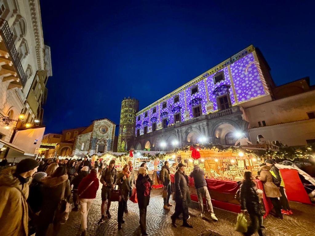 Mercatino di Natale in piazza della Repubblica con persone che si godono l'atmosfera festiva, illuminazione colorata sulle facciate degli edifici e bancarelle decorate.
