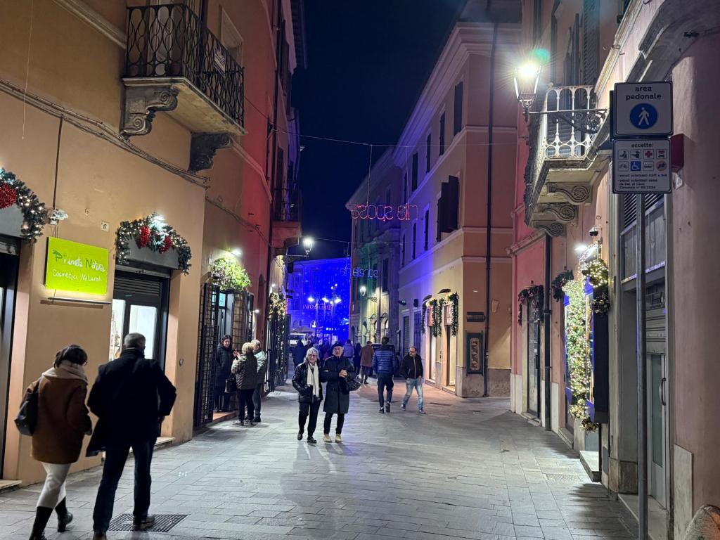 Un vicolo illuminato di notte con alberi di Natale decorati, persone che passeggiano e un'insegna luminosa che dice 'sogni di Natale'.