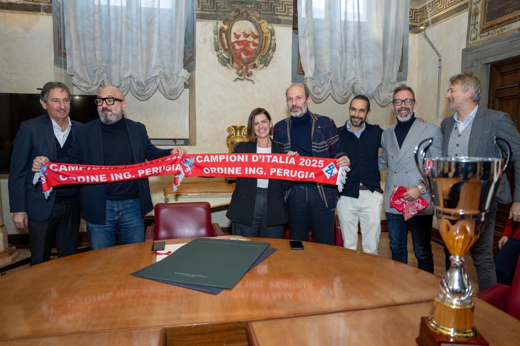 Cerimonia di premiazione della squadra di calcio dell'Ordine degli ingegneri di Perugia, con i membri della squadra e i rappresentanti del comune che mostrano il trofeo e una sciarpa con le scritte 'Campioni d'Italia 2025' e 'Ordine Ing. Perugia'.