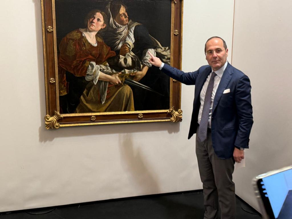 Un curatore indica un dipinto barocco di due figure, evidenziando dettagli dell'opera mentre è esposto in una galleria.