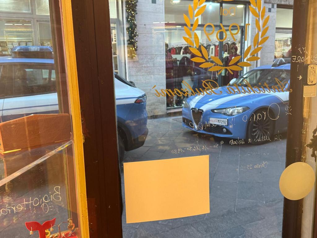 Vista di un negozio con una finestra, che mostra un'auto della polizia blu parcheggiata all'esterno e una sedia all'interno del negozio.