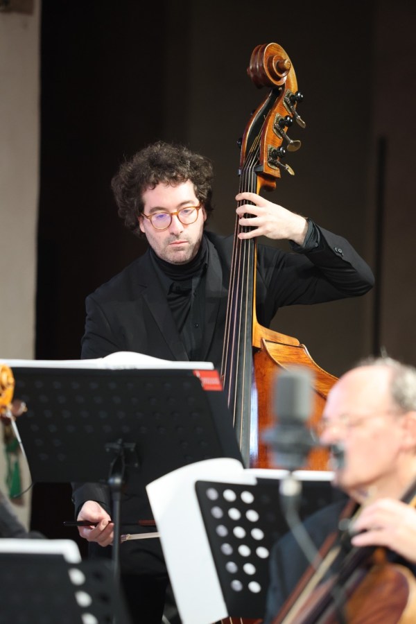 A musician playing a double bass during a performance, with sheet music stands in the foreground.