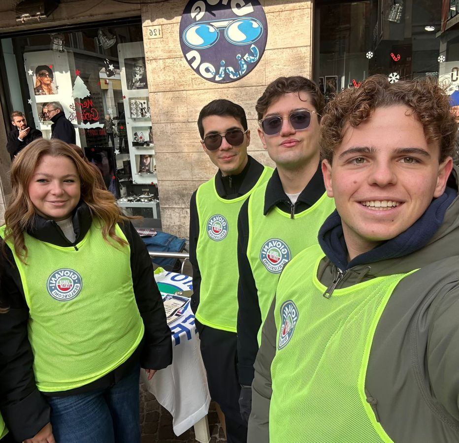 Group of four people wearing bright green vests with logos, smiling at the camera in a city street setting.