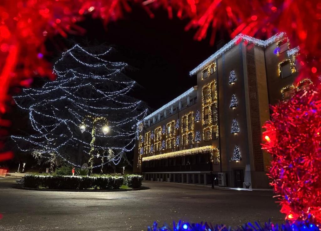 Una vista notturna di un edificio decorato con luci natalizie, circondato da un albero illuminato e un'atmosfera festiva.