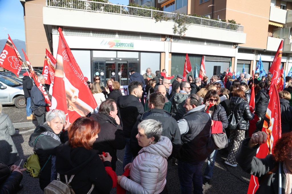 A crowd of people gathered outside a building, holding red flags and banners, participating in a demonstration or rally.