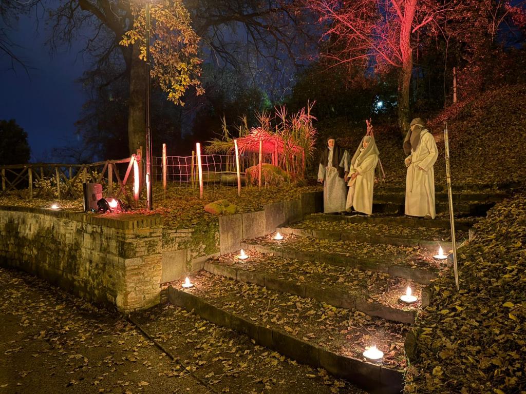 People dressed in traditional robes standing on stone steps lit by candles, surrounded by autumn leaves and trees illuminated with red lights.