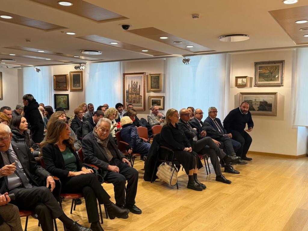 Un gruppo di persone sedute in una sala espositiva, con opere d'arte appese alle pareti. L'atmosfera è rilassata in occasione dell'inaugurazione della mostra 'Collezione d’arte. Da Signorelli a Burri'.