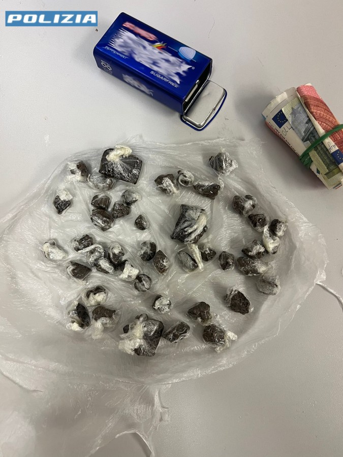 Una busta trasparente contiene 43 involucri di hashish, accanto a un sacchetto blu e una somma di denaro in banconote.