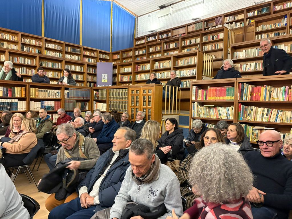 Una sala di lettura affollata durante la presentazione del libro "Pensieri nell’acqua" di Franco Fogliano, con persone sedute e in piedi tra gli scaffali di libri.